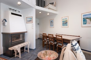 A dining area with a wooden table and chairs, a bench, a fireplace, and a view of the upper floor.