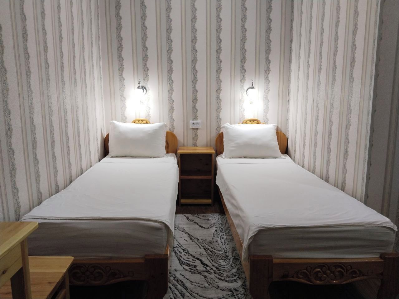 Une chambre avec deux lits simples, des têtes de lit en bois, une petite table de chevet et un tapis à motifs.