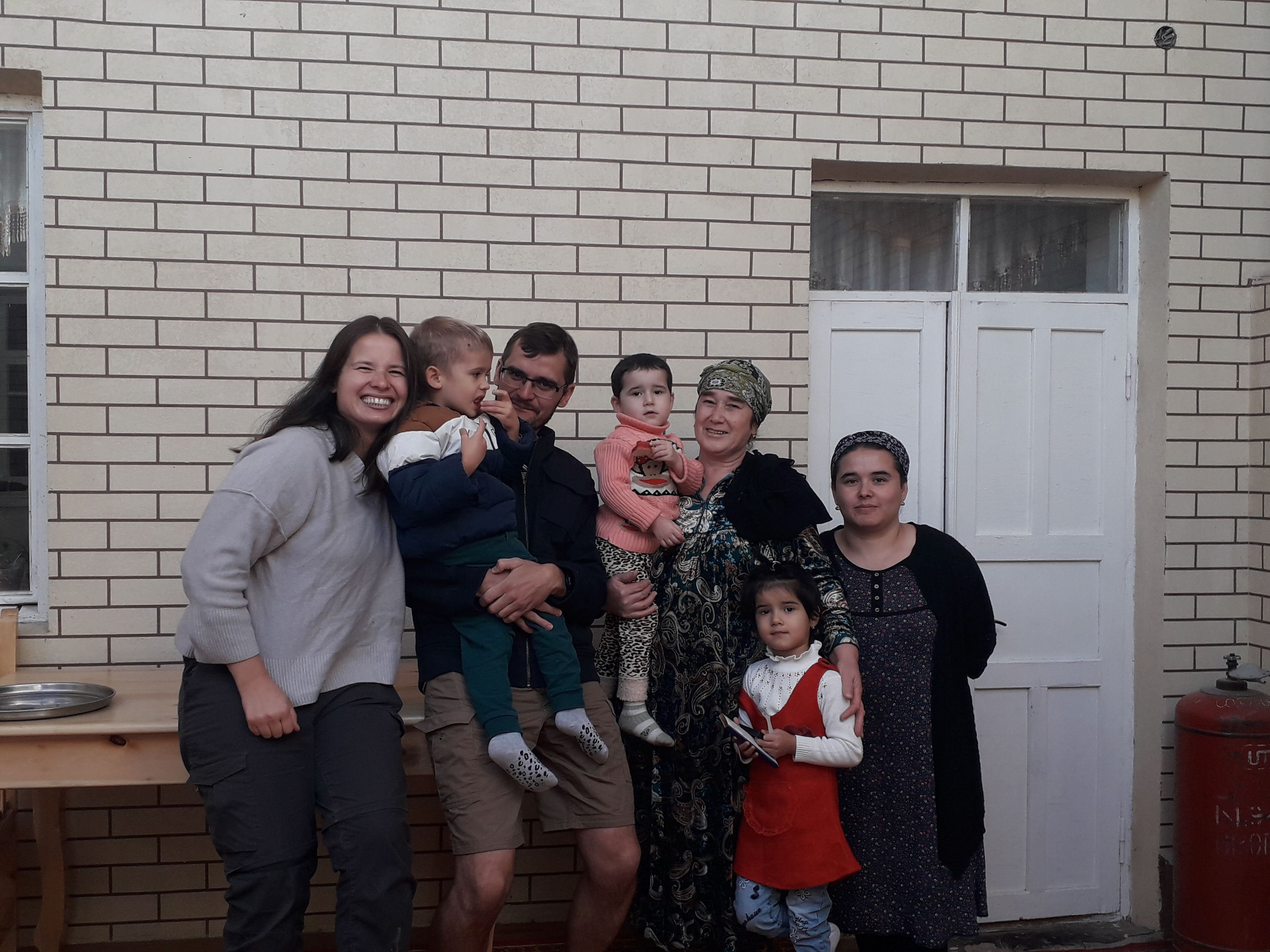 Un grupo de personas de pie frente a un edificio de ladrillo con una puerta blanca y una ventana.