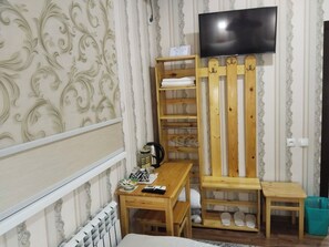 A room with a wooden table, a TV mounted on the wall, and a shoe rack. - Gostevoy dom HOTEL ALLANAZAR OTA (Khiva)