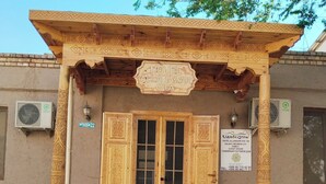 Fachada de hotel con elaboradas tallas de madera, un letrero y dos macetas.
