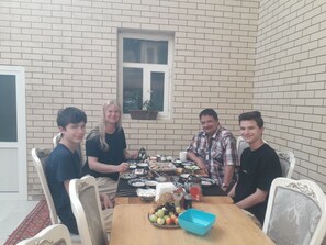 A group of people seated around a wooden dining table with a brick wall background. - Gostevoy dom HOTEL ALLANAZAR OTA (Khiva)