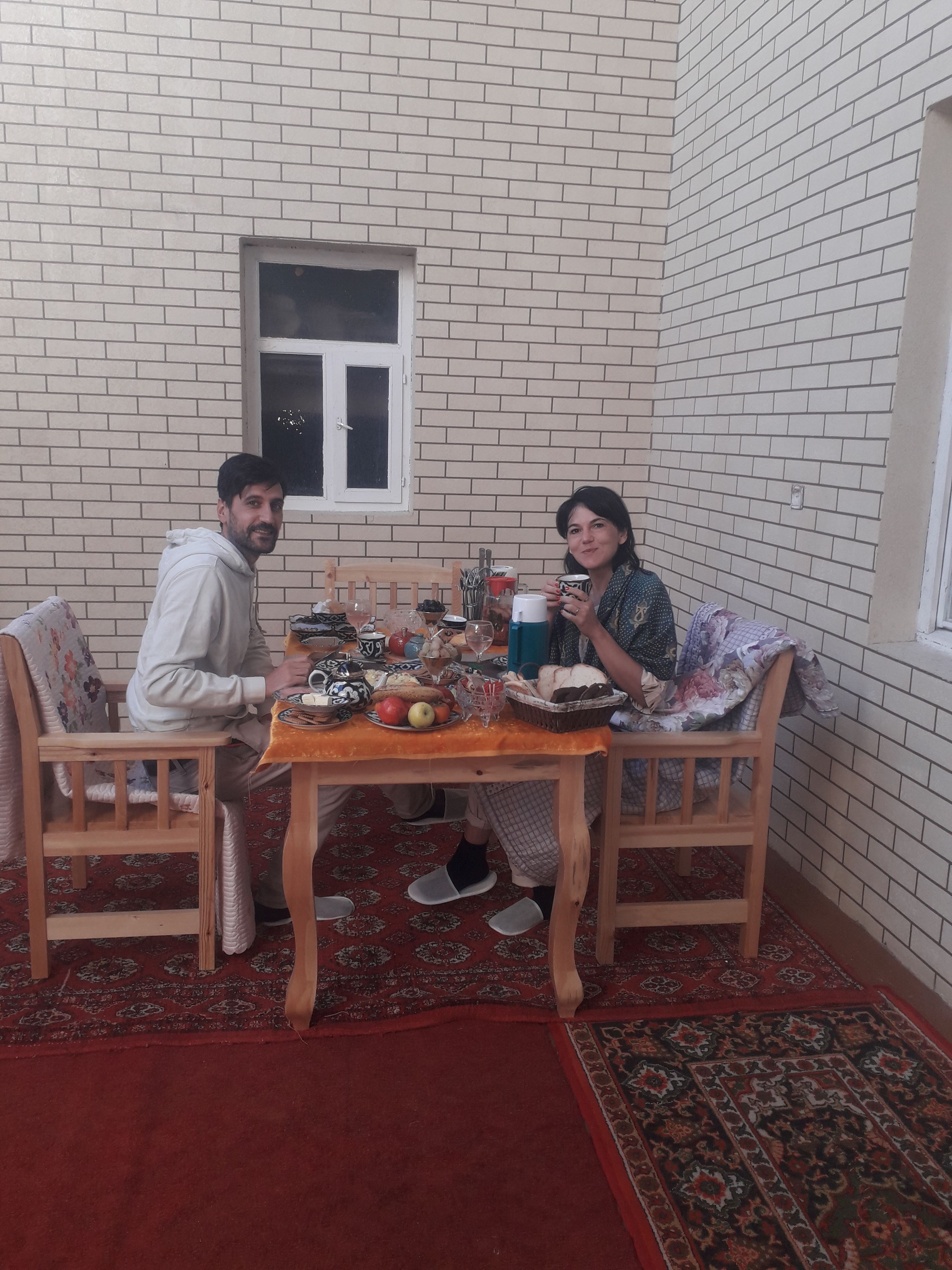 Comedor con pared de ladrillo, una ventana y una mesa servida con comida y bebidas.