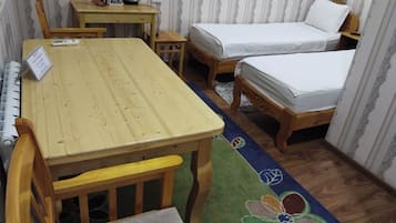 A room with a wooden table, two single beds, a small table with a kettle, and a chair.