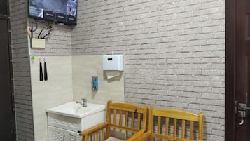 Casa de banho com lavatório branco, cadeiras de madeira, espelho e uma televisão montada a exibir imagens de vigilância.