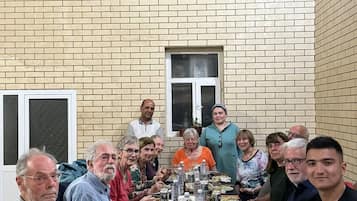 A group of people seated around a long table with various dishes and drinks, in a room with brick walls and a window.