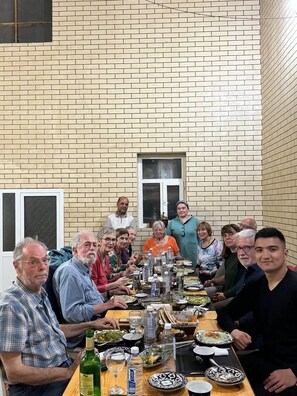 A group of people seated around a long table with various dishes and drinks, in a room with brick walls and a window. - Gostevoy dom HOTEL ALLANAZAR OTA (Khiva)