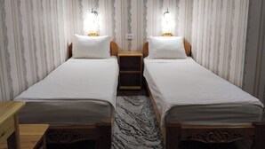 A room with two single beds, wooden headboards, a small bedside table, and a patterned rug. - Gostevoy dom HOTEL ALLANAZAR OTA (Khiva)