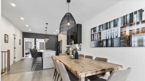 A modern dining area with a wooden table, grey upholstered chairs, and a black pendant light. - Nature, Comfort retreat | La Grande Escapade (Saint-Donat-de-Montcalm)