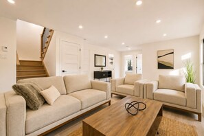 A modern living room with a sofa, armchairs, a coffee table, and a staircase.