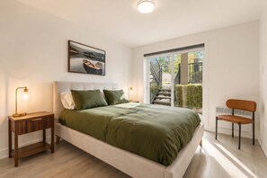 A modern bedroom with a bed, bedside tables, a chair, a window, and a painting. - Nature, Comfort retreat | La Grande Escapade (Saint-Donat-de-Montcalm)