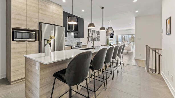 A modern kitchen with a central island, bar stools, pendant lighting, and a view to the dining area. - Nature, Comfort retreat | La Grande Escapade (Saint-Donat-de-Montcalm)