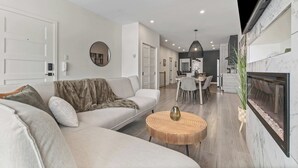 A modern living room with a sofa, a round wooden coffee table, a fireplace, and a dining area in the background. - Nature, Comfort retreat | La Grande Escapade (Saint-Donat-de-Montcalm)