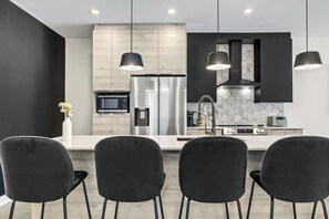A modern kitchen with a central island, black chairs, and pendant lighting.