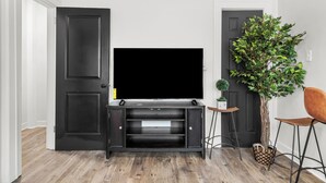 Una habitación con un mueble de entretenimiento negro, un televisor, una planta en maceta y piso de madera.