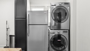 Una cocina compacta con un refrigerador de acero inoxidable, lavadora y secadora de doble puerta, y una mesa de madera.