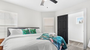 Un dormitorio con cama, ventilador de techo, una puerta y una ventana con persianas.
