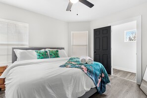 Ein Schlafzimmer mit Bett, Deckenventilator, Tür und Fenster mit Jalousien.
