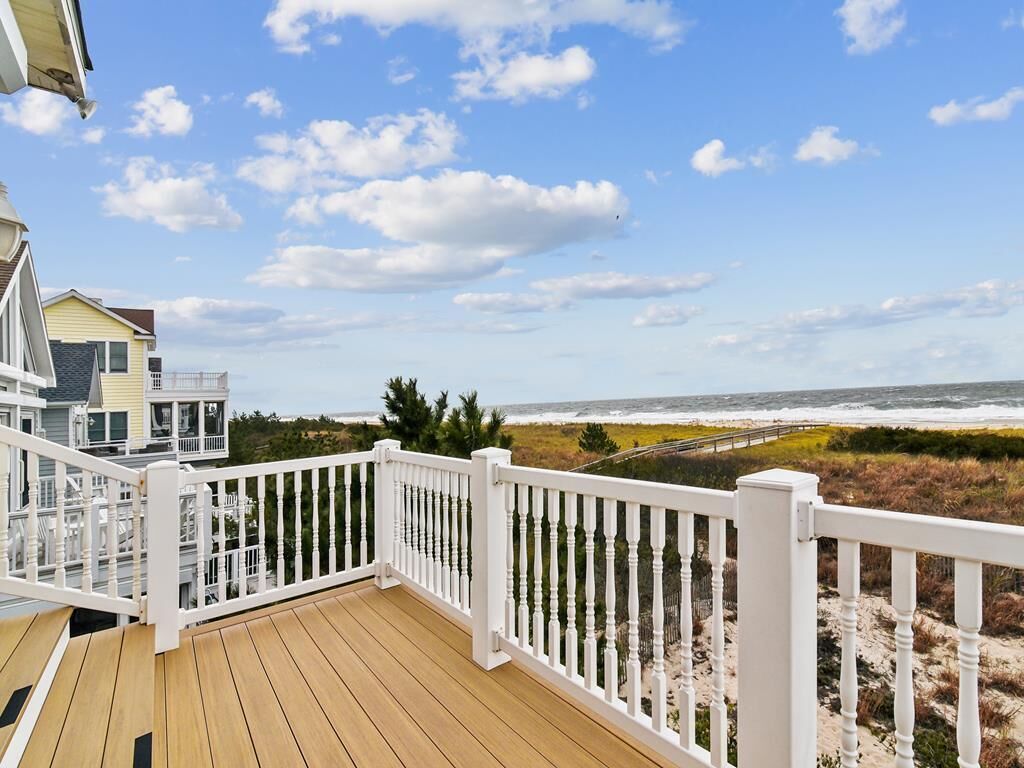 A wooden deck with white railings overlooking a beach with dunes and ocean.