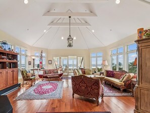 Ein geräumiges Wohnzimmer mit hohen Decken, großen Fenstern und Blick ins Freie.