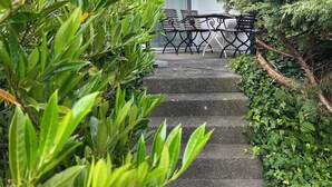 Uma casa com telhado de telhas vermelhas, escadaria que leva a um alpendre e vegetação ao redor.