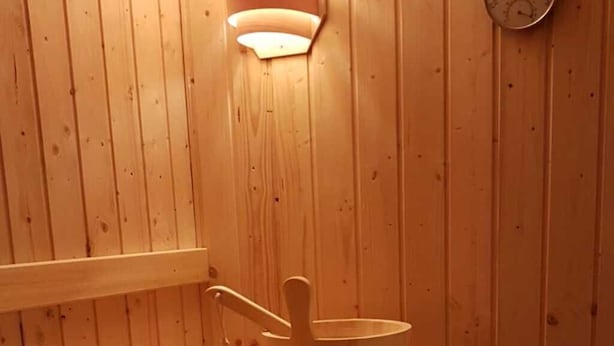 Banco de sauna de madeira com um balde de madeira e um termômetro fixado na parede.