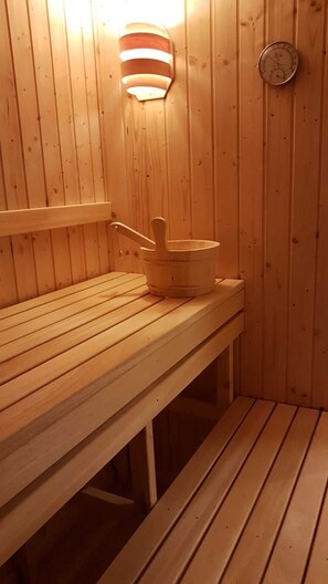 Puinen saunapenkki, puinen ämpäri ja seinälle kiinnitetty lämpömittari.
