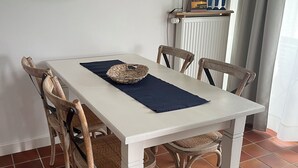Uma mesa de jantar com quatro cadeiras, um jogo americano trançado e uma luminária pendente.