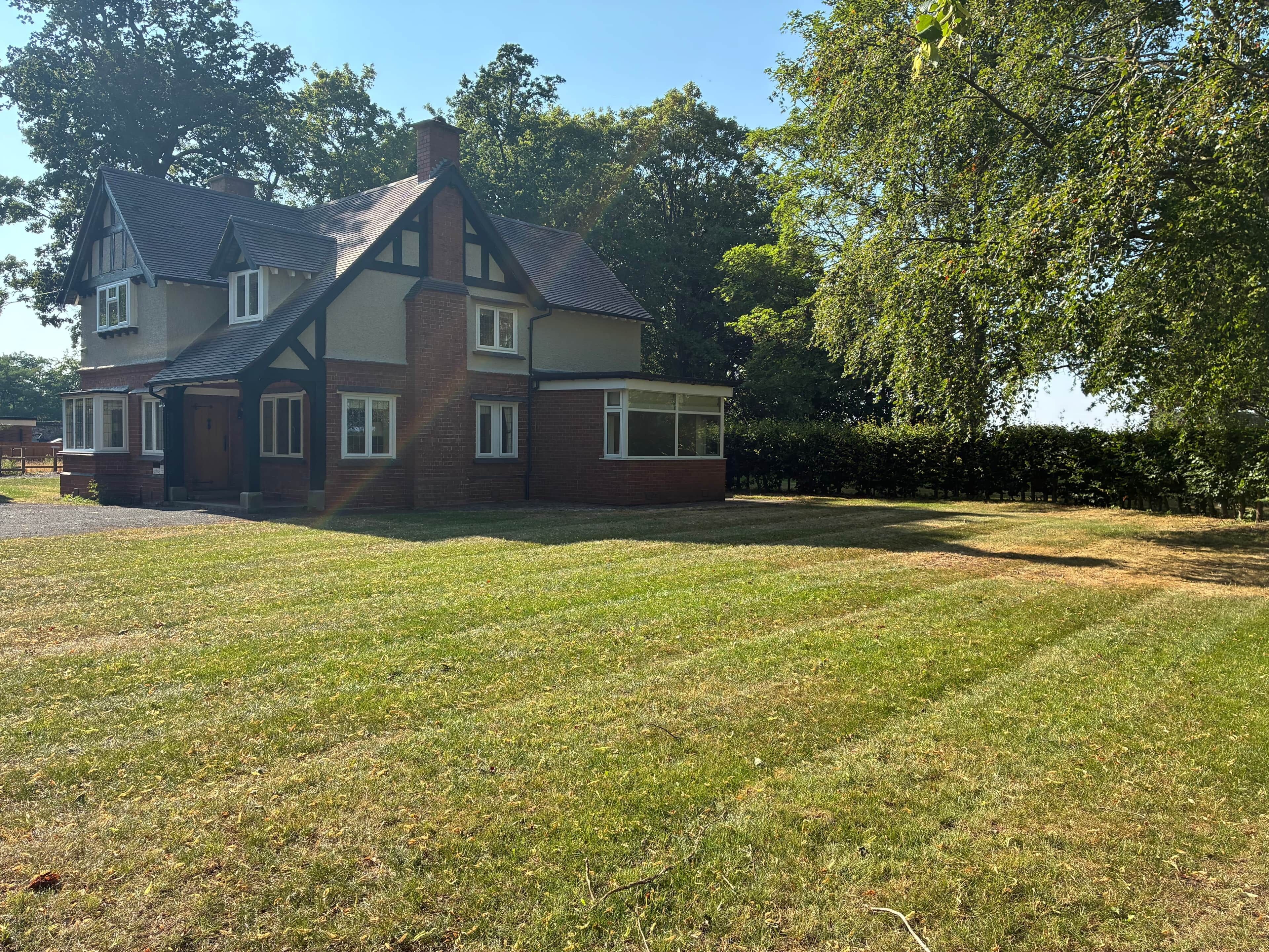A two-story house with a brick facade, multiple windows, and a large lawn.