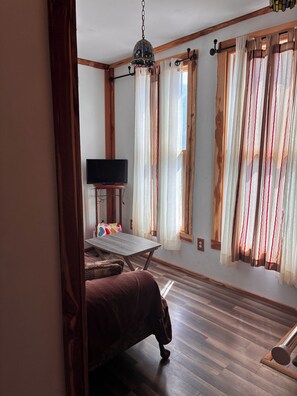 A room with a bed, a television on a stand, a wooden floor, and a window with curtains. - Cozy 1-bedroom cabin in marvelous Tazewell (Tazewell)