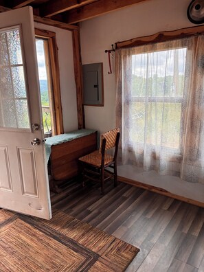 Una habitación con escritorio de madera, una silla, un ventanal con cortinas estampadas y una puerta con panel de vidrio esmerilado.
