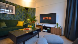 Una sala de estar moderna con un sofá verde, una mesa de centro y un televisor de pantalla plana mostrando 'NETFLIX'.