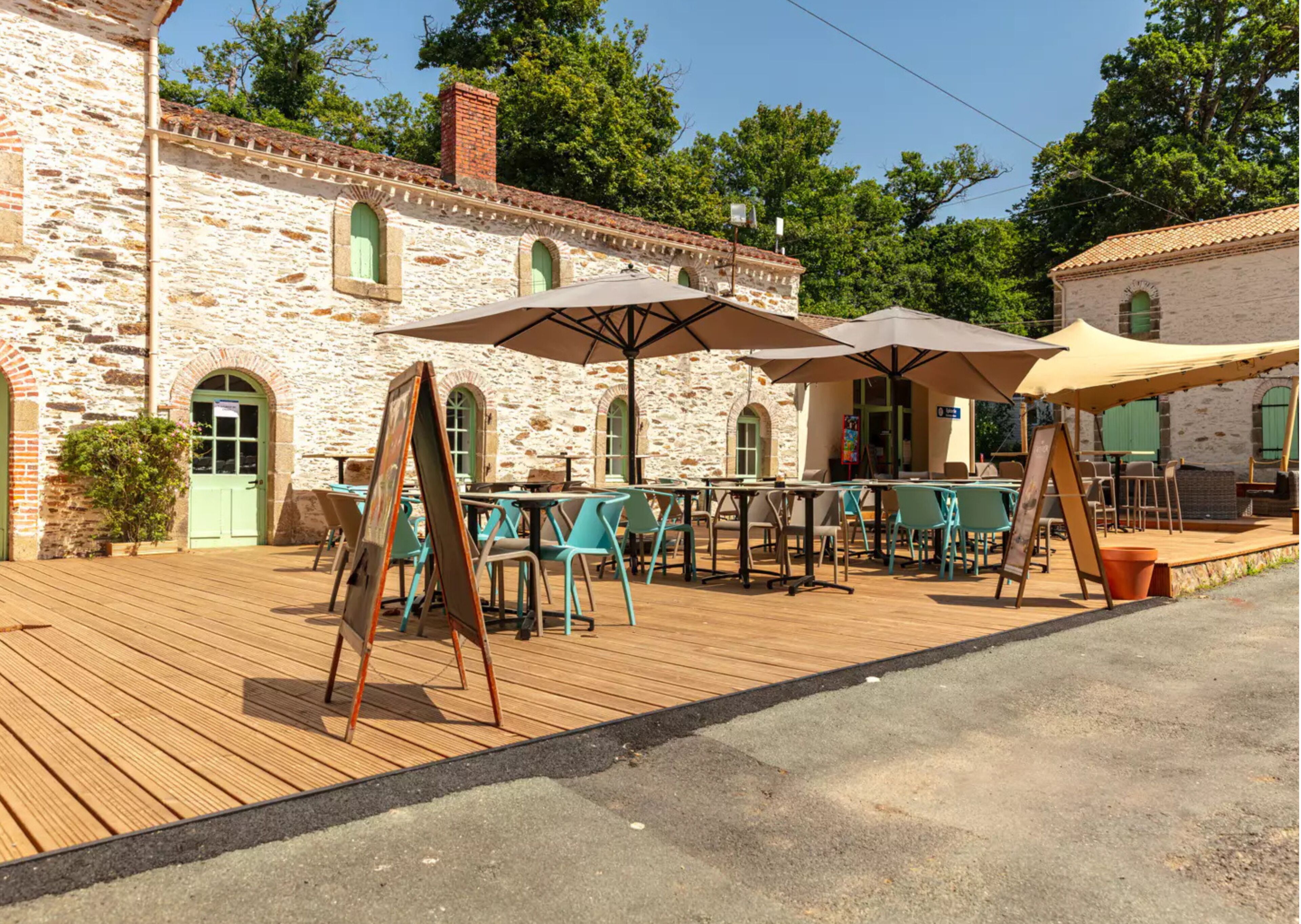 An outdoor seating area with tables and chairs, a stone building with arched windows, and a wooden deck.