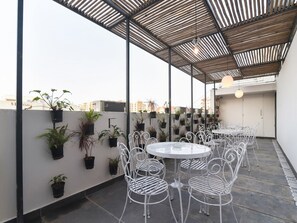 Eine Dachterrasse mit einem runden Tisch und weißen Metallstühlen, umgeben von Topfpflanzen.
