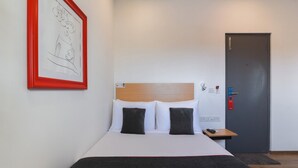 Une chambre d’hôtel avec un lit, une table de chevet, une porte et un tableau encadré au mur.
