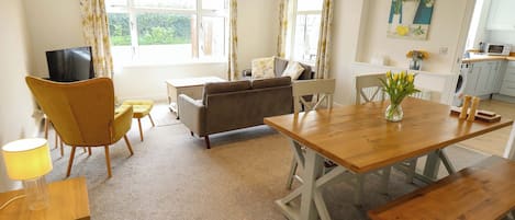A living room with a sofa, a wooden dining table, a TV, and a kitchen area with a microwave.