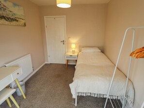 Ein kleines Zimmer mit einem Einzelbett, einem Schreibtisch, einer Heizung und einer Tür.
