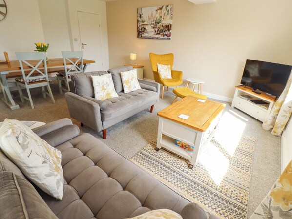 A living room with a sofa, a coffee table, a TV stand, and a dining area with chairs and a table. - Field View (North Walsham)