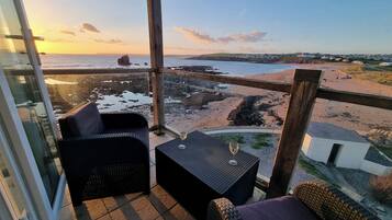 A balcony with wicker furniture, a glass door, and a view of the beach and ocean.