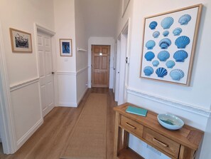 Ein Korridor mit Holzboden, weißen Wänden, einer Holztür und einem gerahmten Bild von Muscheln an der Wand.