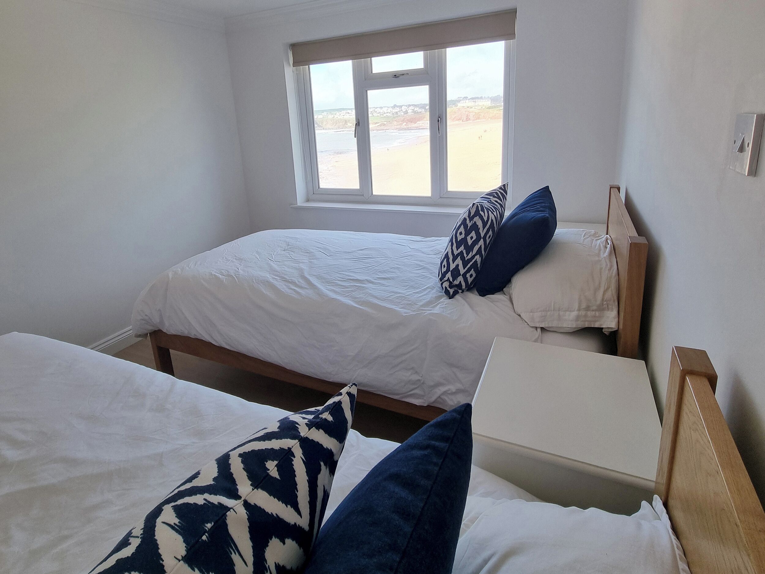 A room with two beds, a window with a view of the beach, and a wooden headboard.