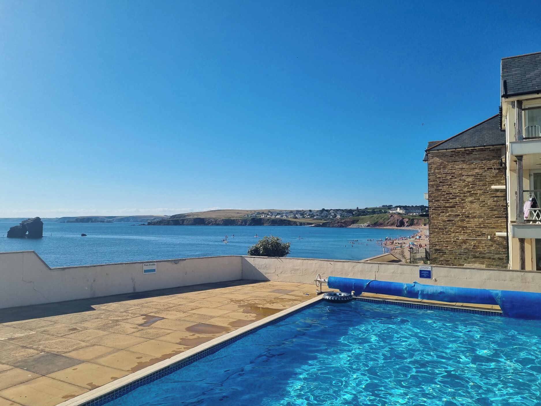 A swimming pool with a view of the sea, a stone building, and a clear sky.