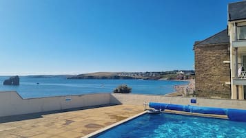 A swimming pool with a view of the sea, a stone building, and a clear sky.