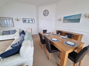 A dining area with a wooden table set for four, a white sofa with patterned cushions, and a framed picture on the wall. - 11 Thurlestone Rock (Kingsbridge)