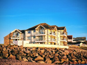 A multi-story building with balconies, situated on a rocky shoreline. - 11 Thurlestone Rock (Kingsbridge)