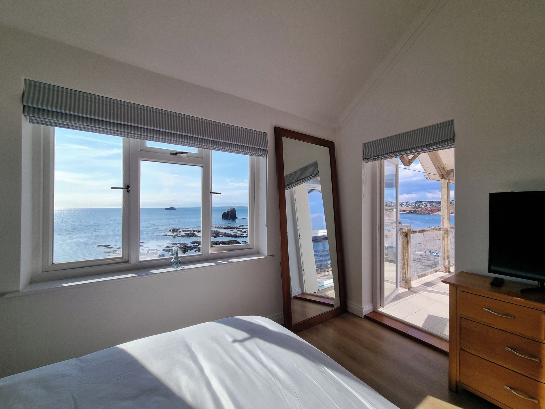 A bedroom with a bed, a dresser, a TV, and a large window with a view of the sea and a ship.