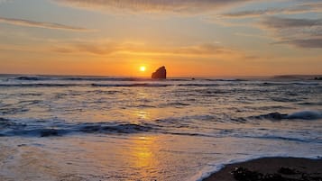 Um pôr do sol sobre o oceano com ondas e uma formação rochosa.