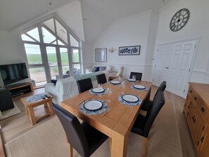 A dining area with a wooden table set for six, black chairs, a clock on the wall, and a TV in the corner. - 11 Thurlestone Rock (Kingsbridge)