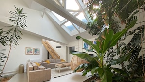 A spacious living area with a high ceiling, a staircase, and a large window.