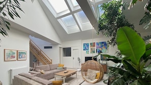 A spacious living area with a high ceiling, a sofa set, a hanging chair, and a large plant.